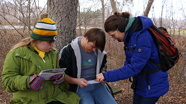 Two students and an education examine a piece of wood, comparing it to their chart.