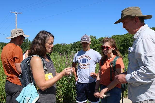 Kim Forbeck, Manager of Land Stewardship, is explaining a plant that she is holding to a group of adults.
