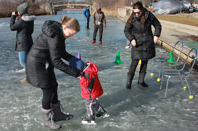 Kid ice skating with adult holding their hands.