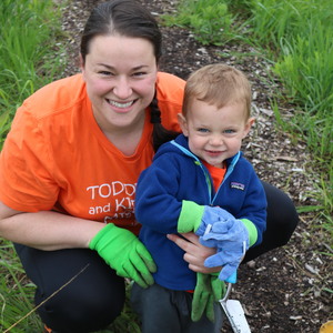 Adult and child wearing gardening gloves smile at the camera.