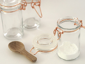 Two clear glass jars. One has a powder in it. Small wooden measuring spoon lays in front.